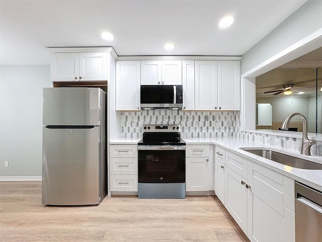 kitchen featuring stainless steel appliances, tasteful backsplash, light wood-style floors, white cabinets, and a sink