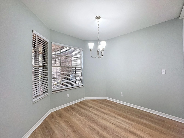 spare room with an inviting chandelier, wood finished floors, and baseboards