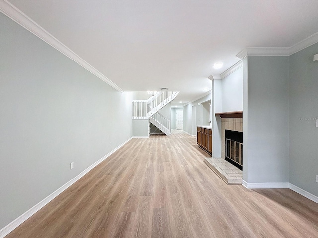 unfurnished living room with a tile fireplace, light wood-style flooring, baseboards, stairs, and crown molding