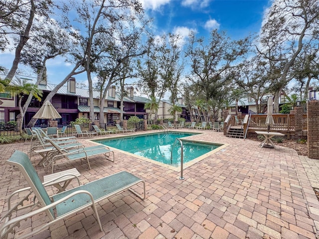 community pool featuring a patio, a wooden deck, and fence