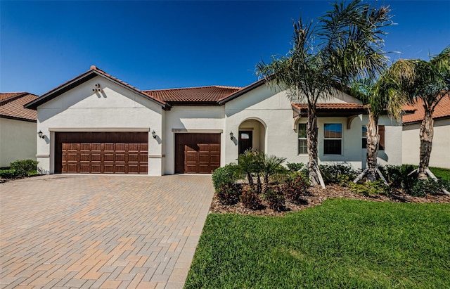 mediterranean / spanish-style house with decorative driveway, a tile roof, stucco siding, a front yard, and a garage