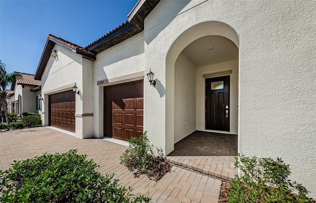 view of exterior entry featuring a tiled roof, decorative driveway, an attached garage, and stucco siding