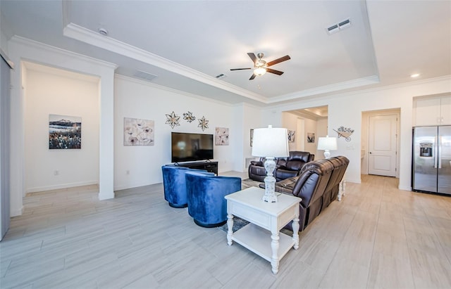 living area featuring ceiling fan, visible vents, light wood-style floors, ornamental molding, and a tray ceiling