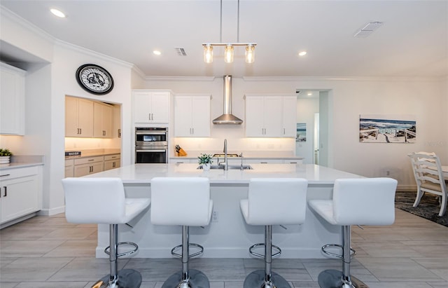 kitchen featuring light countertops, visible vents, double oven, wall chimney range hood, and a kitchen bar