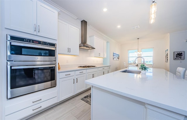 kitchen with a sink, visible vents, light countertops, wall chimney range hood, and appliances with stainless steel finishes