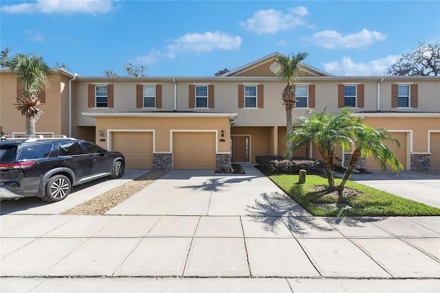 multi unit property with stone siding, stucco siding, driveway, and a garage