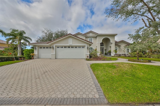 mediterranean / spanish-style house with a garage, stucco siding, decorative driveway, and a front yard