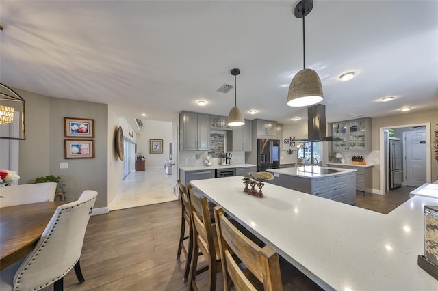 kitchen featuring refrigerator with ice dispenser, visible vents, gray cabinets, decorative backsplash, and island exhaust hood