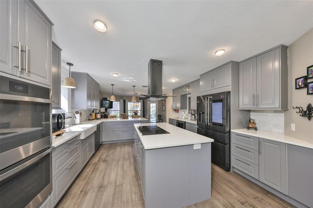 kitchen featuring island exhaust hood, gray cabinetry, appliances with stainless steel finishes, a sink, and a peninsula