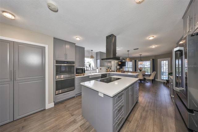 kitchen featuring dark wood-style floors, island exhaust hood, stainless steel appliances, gray cabinets, and light countertops