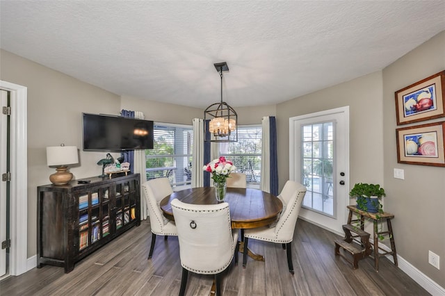 dining space featuring a textured ceiling, a notable chandelier, dark wood finished floors, and baseboards