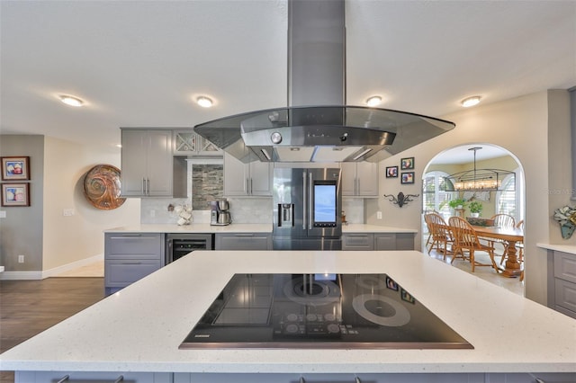 kitchen featuring stainless steel fridge with ice dispenser, gray cabinets, black electric cooktop, and island range hood