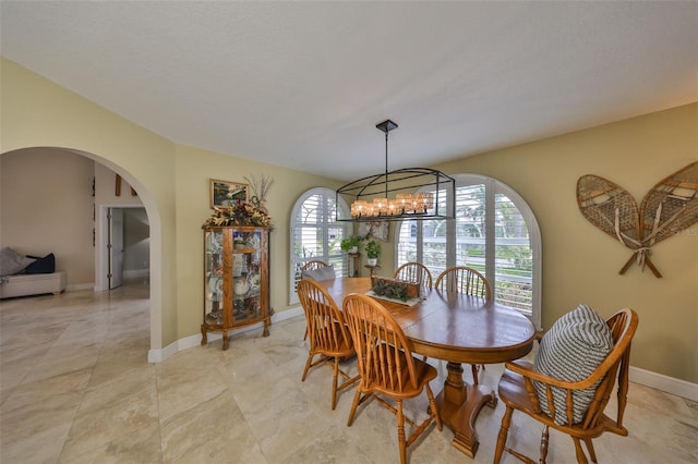 dining room with a healthy amount of sunlight, baseboards, arched walkways, and a notable chandelier