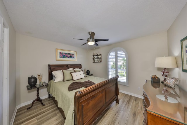 bedroom featuring light wood finished floors, ceiling fan, baseboards, and a textured ceiling