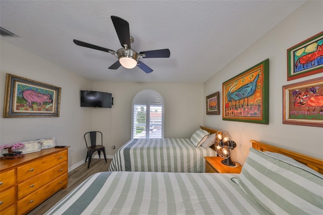 bedroom with ceiling fan, a textured ceiling, wood finished floors, visible vents, and baseboards