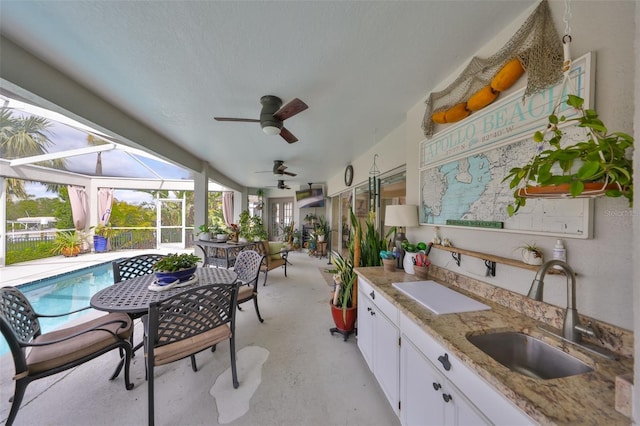 view of patio / terrace with glass enclosure, a sink, ceiling fan, exterior kitchen, and an outdoor pool