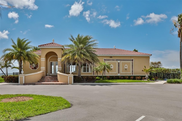 mediterranean / spanish home with stucco siding, a tiled roof, fence, and french doors