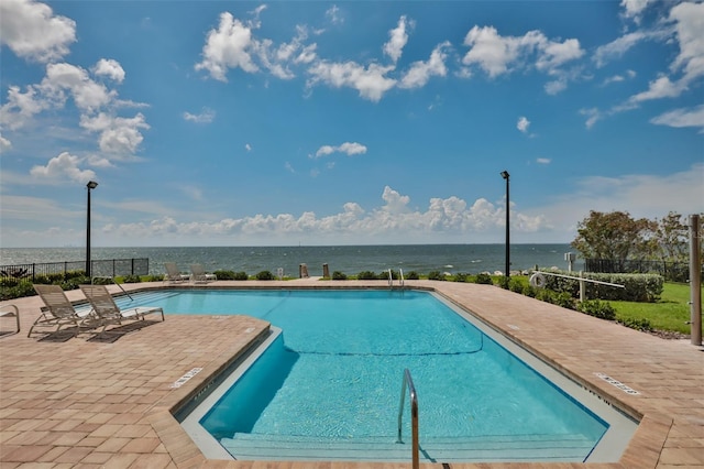 pool with a water view, a patio area, and fence