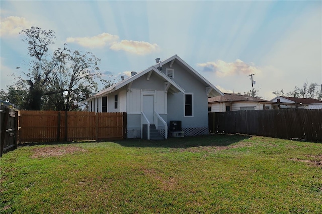 back of house with entry steps, a fenced backyard, and a lawn