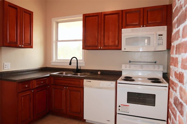 kitchen with dark countertops, light tile patterned flooring, a sink, dark brown cabinets, and white appliances