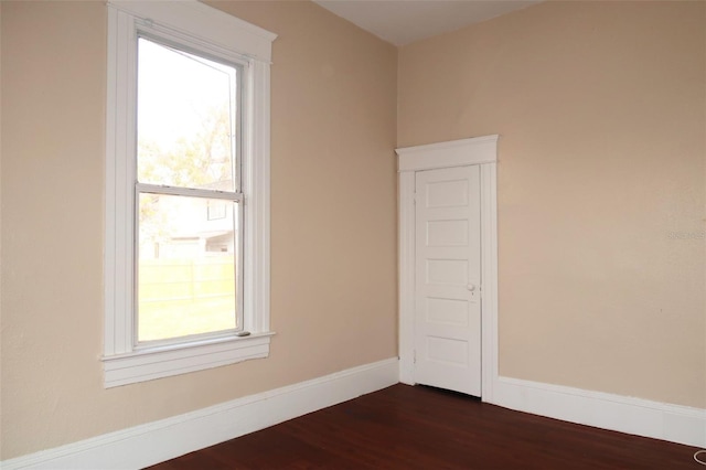 spare room featuring dark wood-type flooring, plenty of natural light, and baseboards