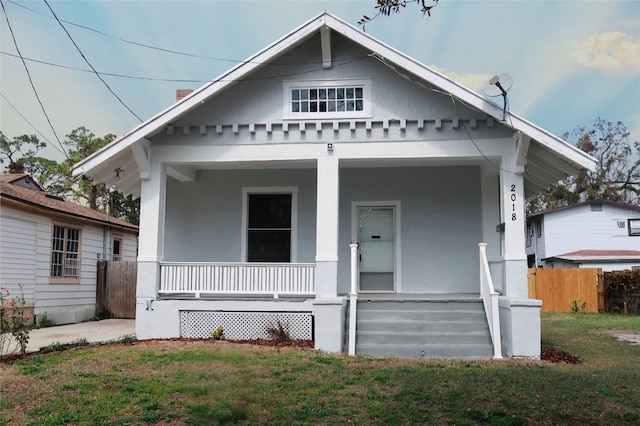 bungalow-style home featuring covered porch, a front lawn, fence, and stucco siding