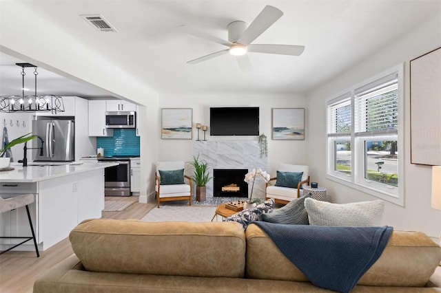 living room featuring visible vents, a fireplace, light wood-style flooring, and ceiling fan with notable chandelier