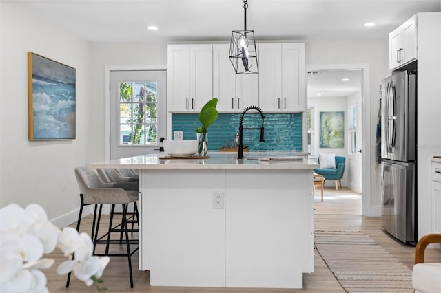 kitchen featuring a breakfast bar area, white cabinets, freestanding refrigerator, decorative backsplash, and light wood finished floors