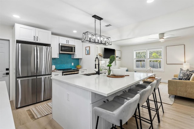 kitchen featuring appliances with stainless steel finishes, a sink, light wood-style flooring, and decorative backsplash