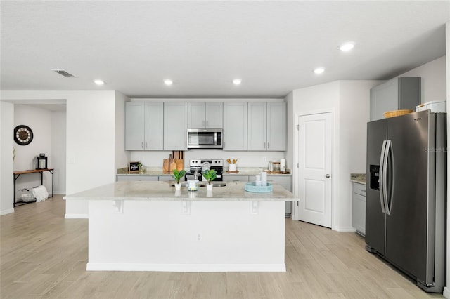 kitchen featuring light stone counters, stainless steel appliances, gray cabinets, visible vents, and a kitchen island