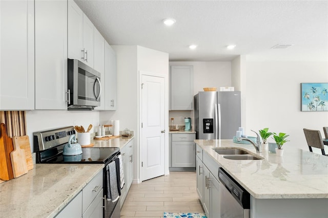 kitchen with light stone counters, light wood-style flooring, stainless steel appliances, a sink, and a center island with sink