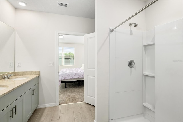 full bathroom with a shower, double vanity, visible vents, a sink, and wood finished floors