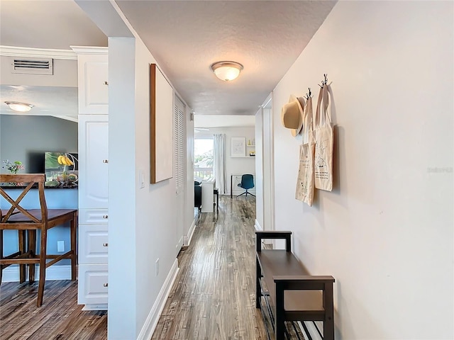 hallway with baseboards, visible vents, and wood finished floors