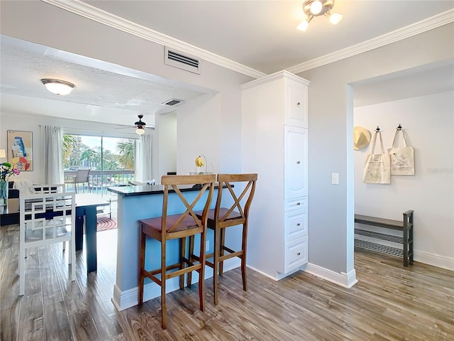 kitchen featuring baseboards, crown molding, visible vents, and wood finished floors