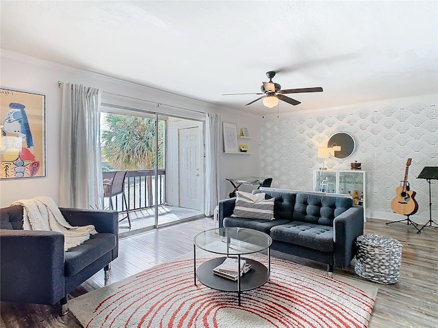 living area with ceiling fan, an accent wall, wood finished floors, baseboards, and wallpapered walls