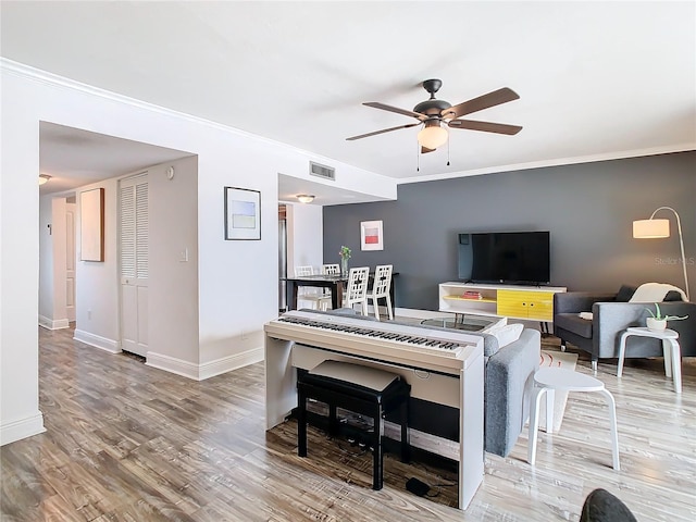 living room featuring ceiling fan, wood finished floors, visible vents, baseboards, and crown molding