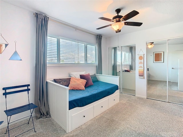 bedroom with a ceiling fan, two closets, and light colored carpet