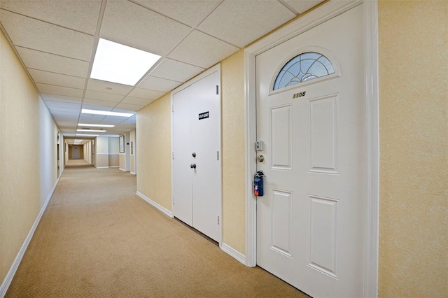 interior space with baseboards, a drop ceiling, and light colored carpet