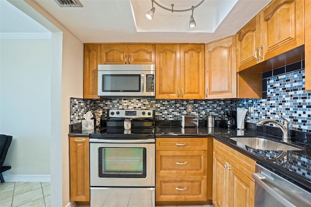 kitchen with a raised ceiling, dark stone counters, appliances with stainless steel finishes, a sink, and backsplash