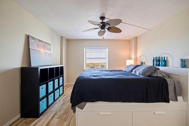 bedroom featuring baseboards, ceiling fan, a textured ceiling, and light wood finished floors