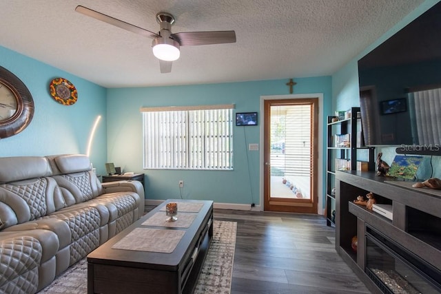 living room featuring ceiling fan, a textured ceiling, baseboards, and wood finished floors