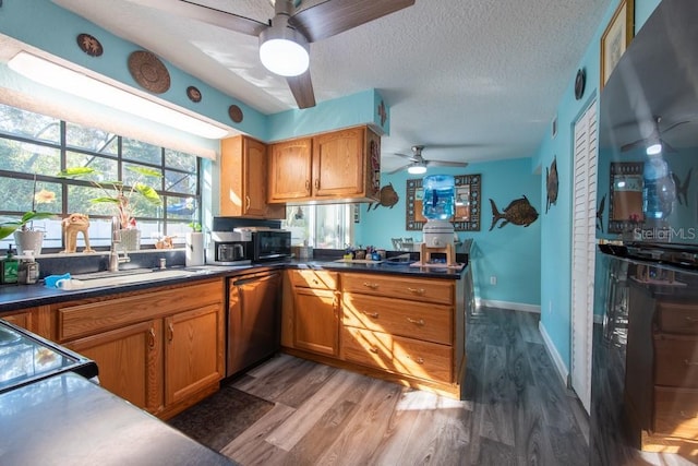 kitchen with brown cabinets, stainless steel dishwasher, a sink, a textured ceiling, and wood finished floors