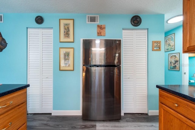 kitchen with visible vents, dark wood finished floors, dark countertops, freestanding refrigerator, and a textured ceiling