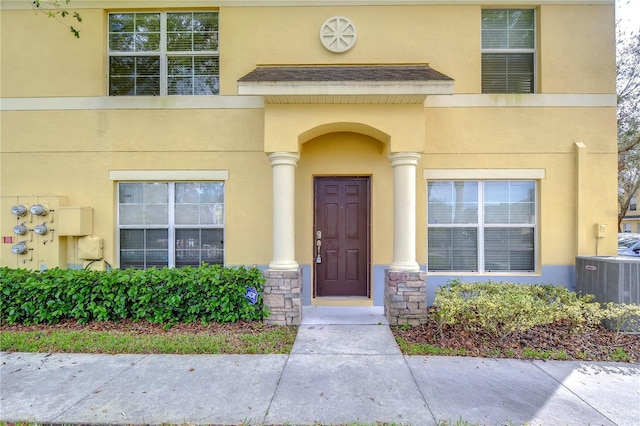 property entrance with stone siding, cooling unit, and stucco siding