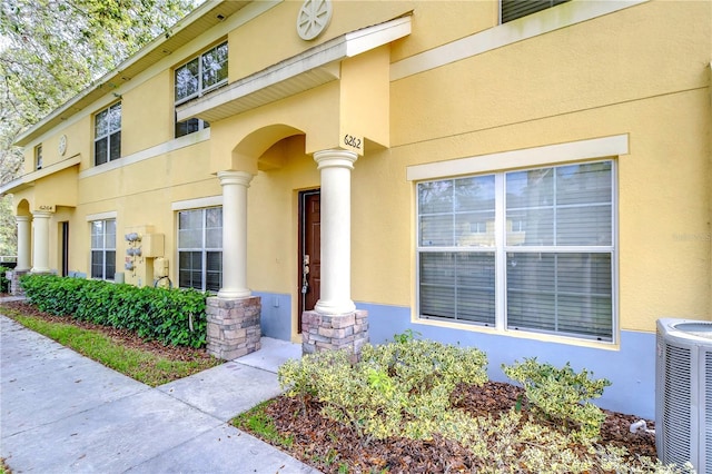 property entrance featuring stone siding, central AC unit, and stucco siding