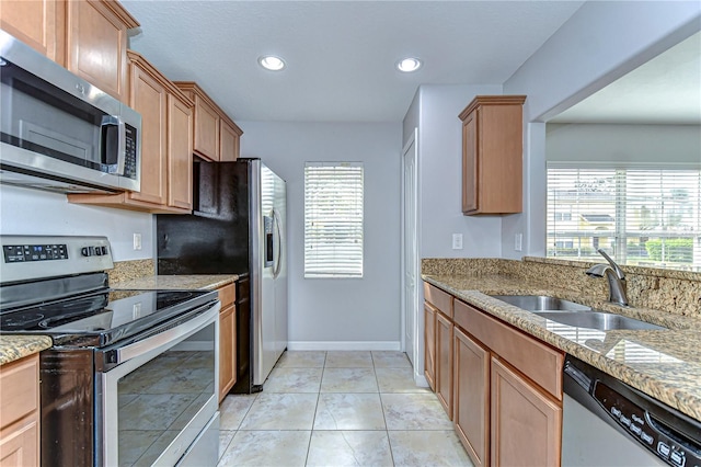 kitchen featuring light tile patterned floors, baseboards, appliances with stainless steel finishes, light stone counters, and a sink