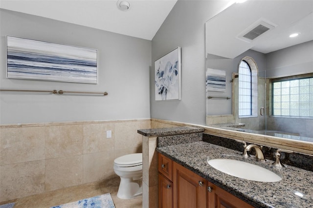 bathroom featuring visible vents, wainscoting, toilet, a shower stall, and tile walls