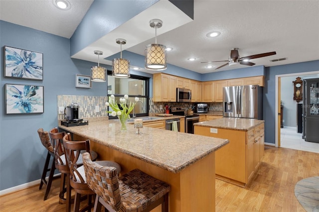 kitchen featuring visible vents, appliances with stainless steel finishes, a center island, a peninsula, and backsplash