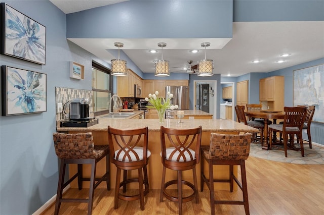 kitchen featuring appliances with stainless steel finishes, light wood-type flooring, a sink, and a peninsula