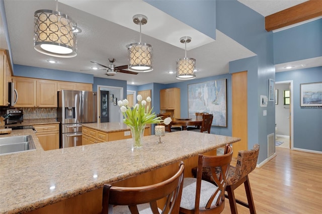 kitchen featuring stainless steel appliances, baseboards, light wood-style floors, a kitchen breakfast bar, and light brown cabinetry